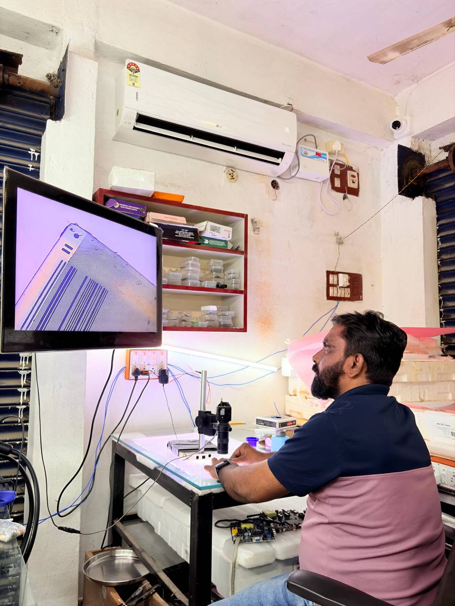 Technician inspecting a panel edge on a large monitor connected to a microscope camera